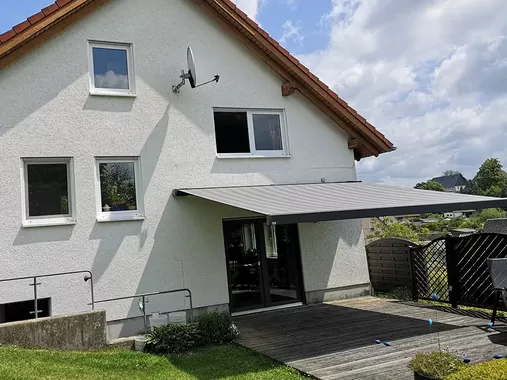 Terrassenmarkise an einem Einfamilienhaus sorgt für angenehmen Schatten im Sitzbereich vor dem Haus