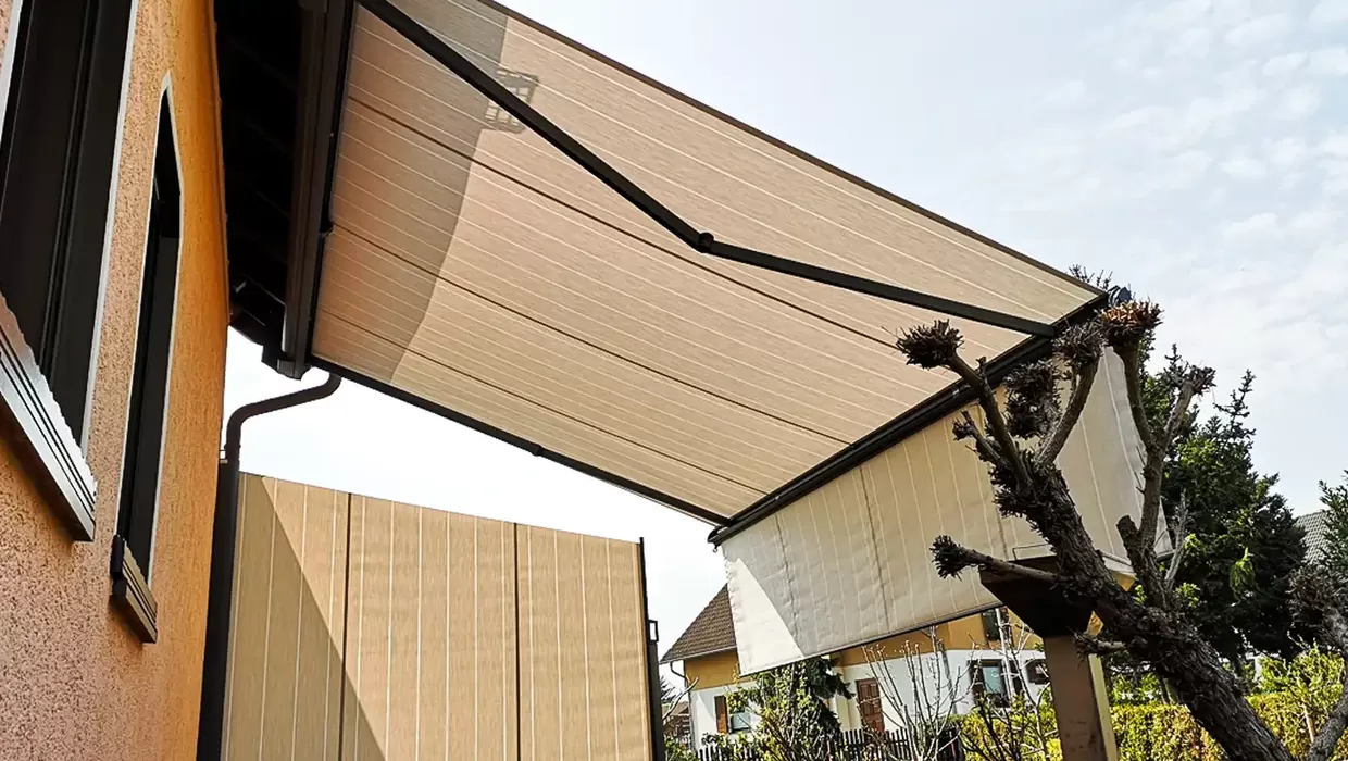 Gelenkarmmarkise an einer Hausfassade spendet Schatten auf der Terrasse und schützt vor direkter Sonneneinstrahlung