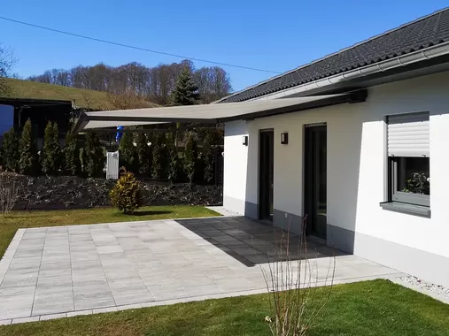 Moderne Terrassenmarkise an einem Einfamilienhaus spendet Schatten auf der Terrasse und schützt vor Sonne