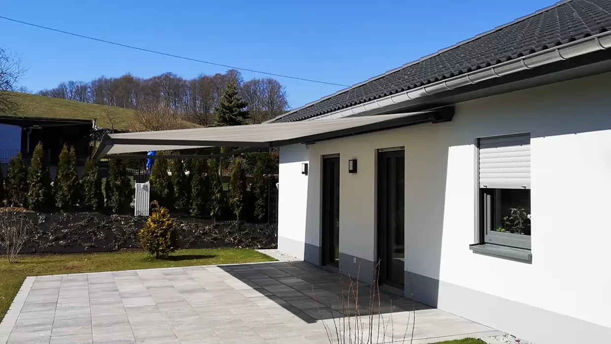 Moderne Terrassenmarkise an einem Einfamilienhaus spendet Schatten auf der Terrasse und schützt vor Sonne