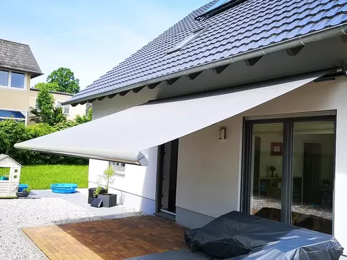 Moderne Gelenkarmmarkise an einem Einfamilienhaus schützt Terrasse und Fenster vor direkter Sonneneinstrahlung